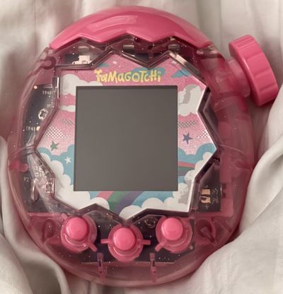 Tamagotchi Paradise in a translucent dark pink glitter shell with hot pink buttons, spinner knob, and flip-top cover.